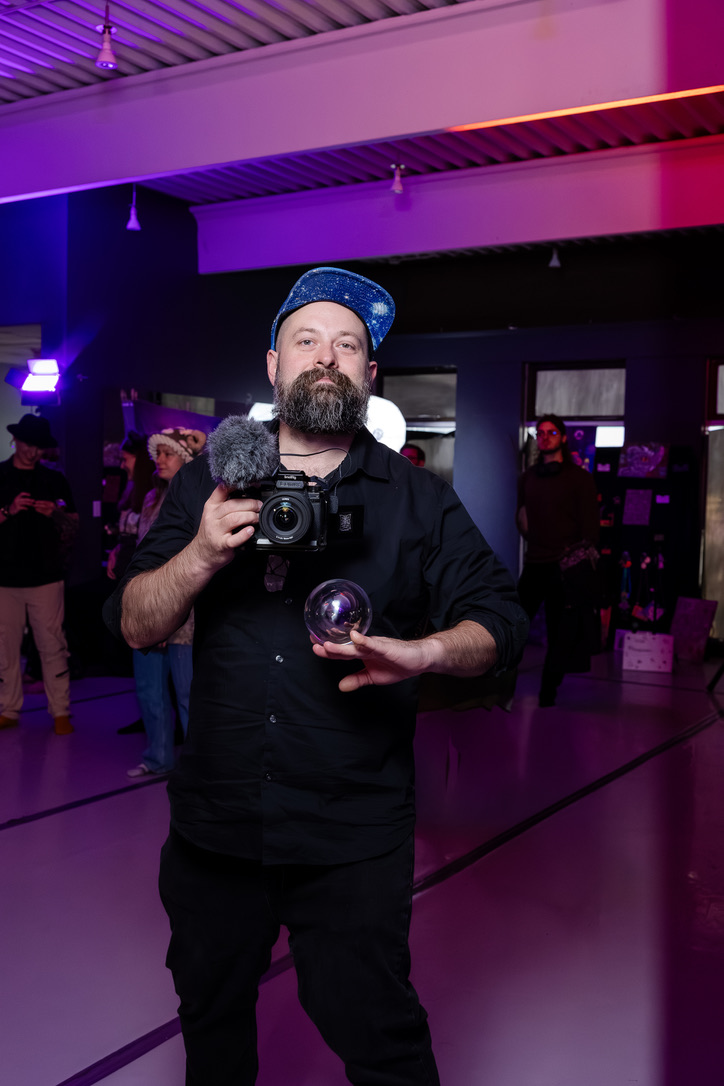 Kia holding a camera and glass sphere in purple event light.